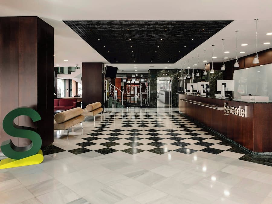 A hotel lobby with a checkered floor, a reception desk, and a large S-shaped letter decoration.