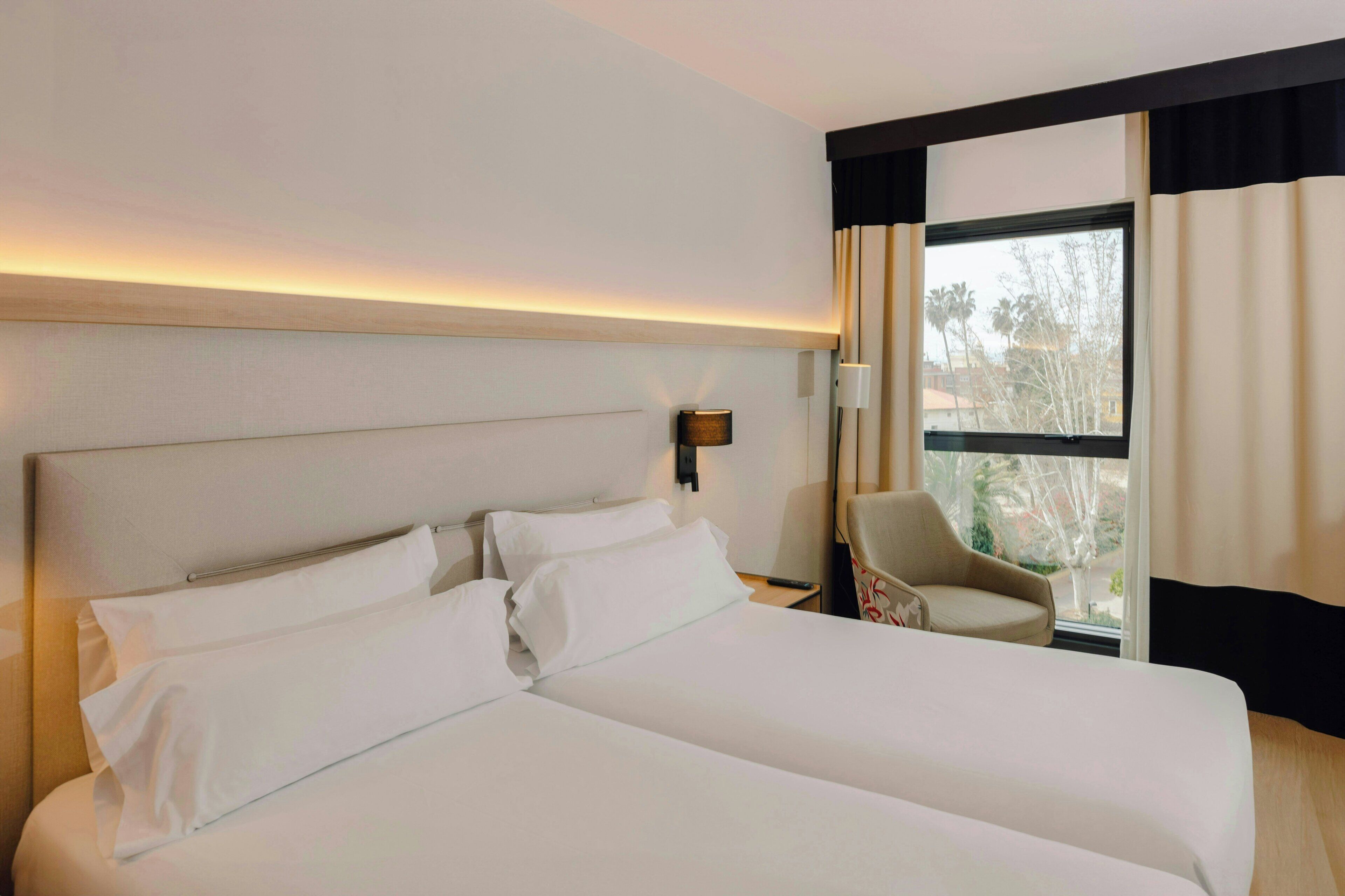 Habitación de hotel con una cama grande, una silla, una mesita de noche y una ventana con cortinas.