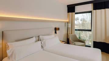 Habitación de hotel con una cama grande, una silla, una mesita de noche y una ventana con cortinas.