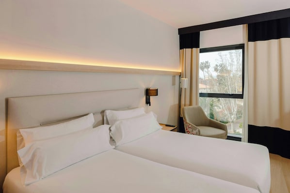 Habitación de hotel con una cama grande, una silla, una mesita de noche y una ventana con cortinas.