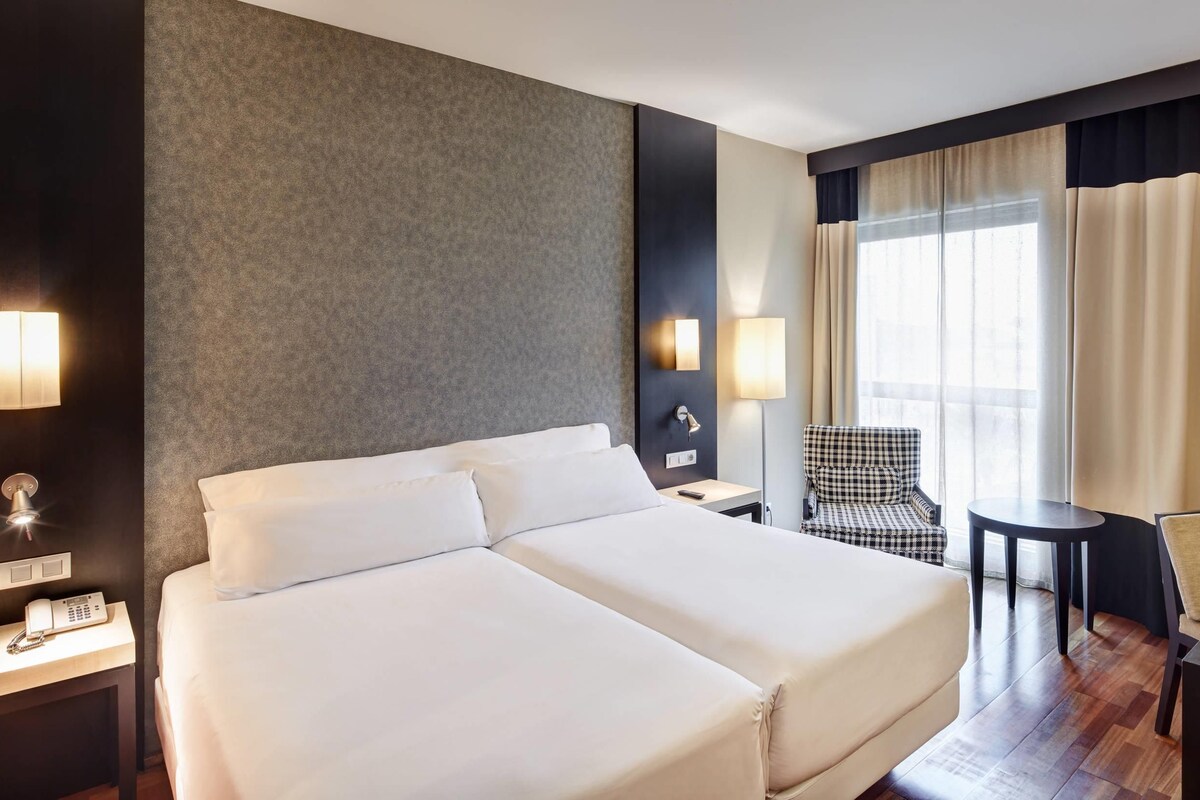 Una habitación de hotel con una cama grande, un escritorio, una silla y una lámpara.