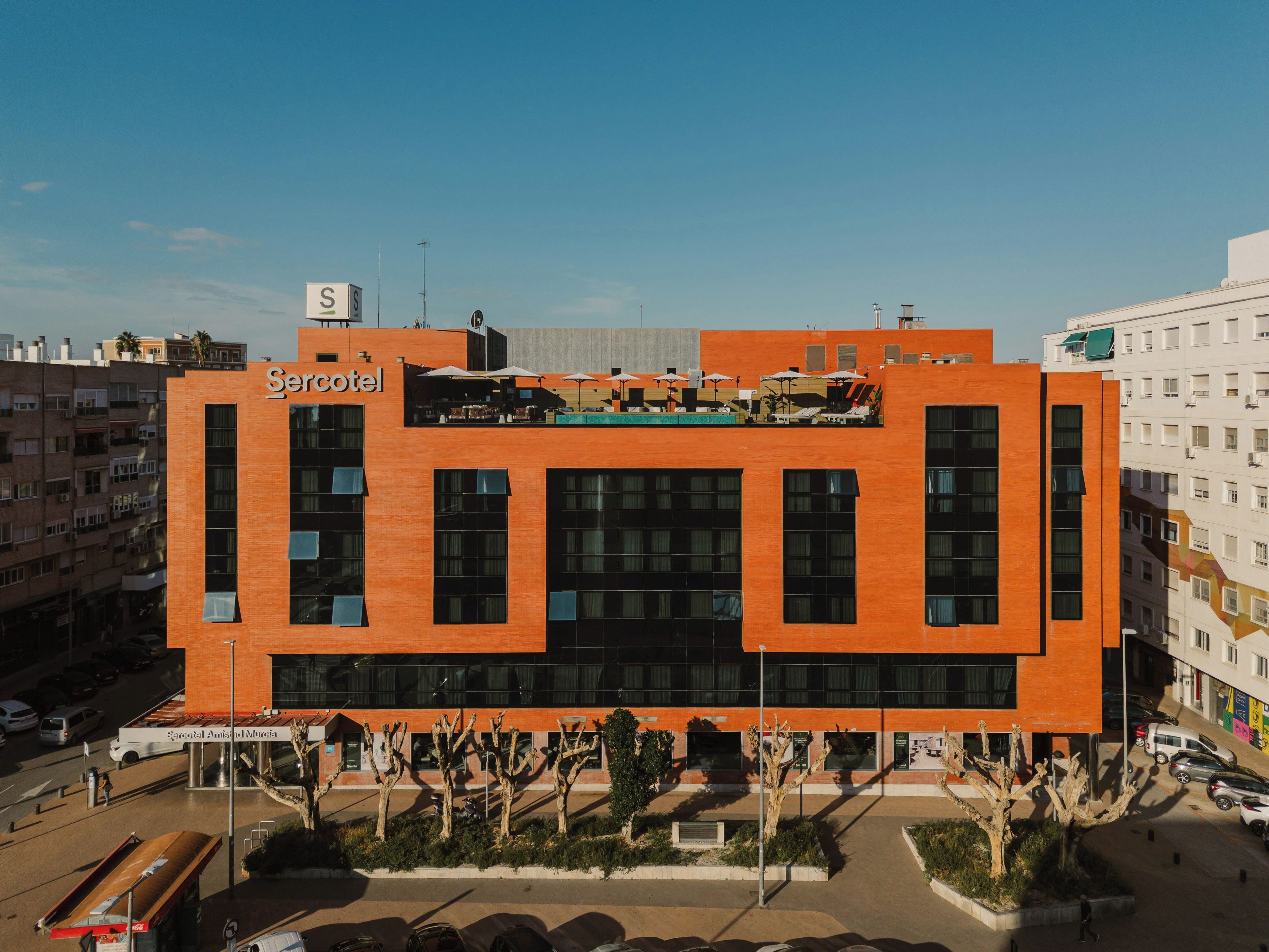 Un hotel moderno con un llamativo letrero 'Sercotel', grandes ventanales y una terraza en la azotea.