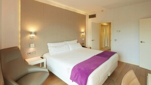 Una habitación de hotel con una cama, una silla, una mesita de noche y un tocador.