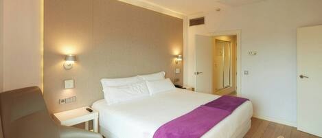 Una habitación de hotel con una cama, una silla, una mesita de noche y un tocador.