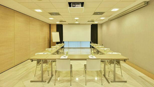 Una sala de conferencias con una larga mesa, sillas, una pantalla de proyector y una pizarra.