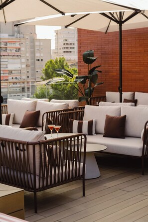 Un espacio al aire libre con mobiliario de mimbre y un muro de ladrillo de fondo.