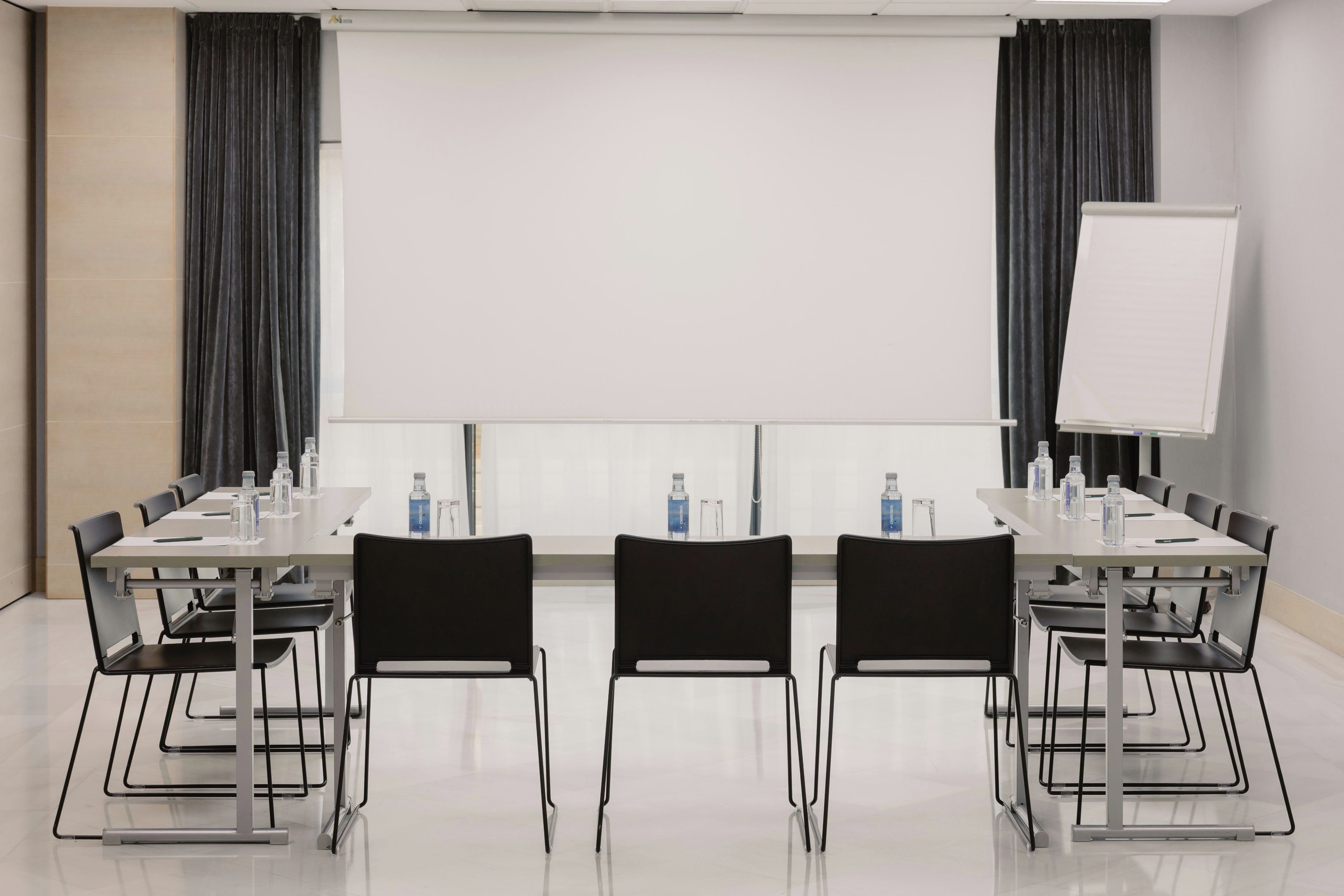 Een vergaderruimte met een whiteboard, een projectiescherm en een lange tafel met stoelen.