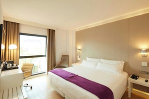 Habitación de hotel con cama, escritorio, silla, mesitas de noche y ventana.
