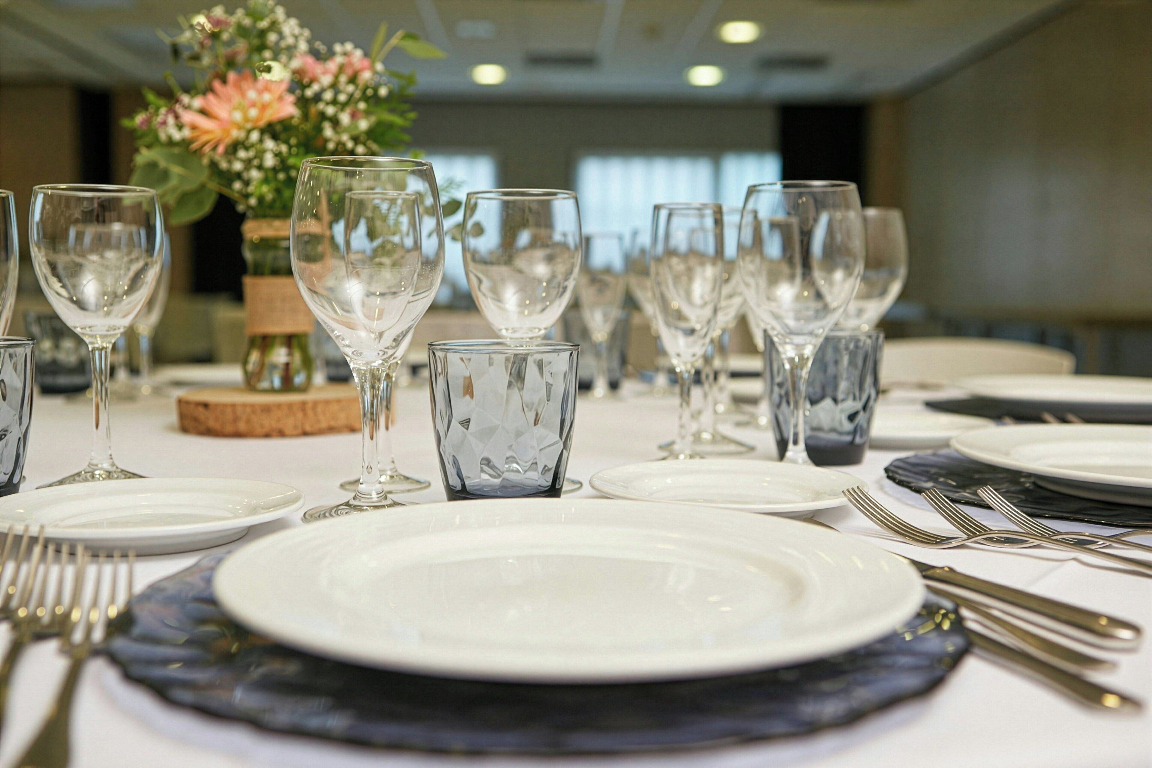A dining table set with white plates, clear wine glasses, and silver cutlery.