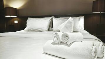 A neatly made bed with white linens and towels, two bedside lamps, and a plain wall.