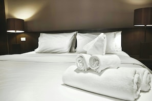 A neatly made bed with white linens and towels, two bedside lamps, and a plain wall. - Sercotel Amistad Murcia (Murcia)