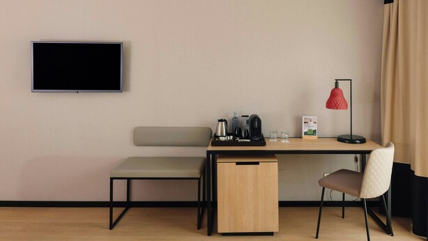 Una habitación moderna con televisión de pantalla plana, un escritorio con silla, un banco y un mueble pequeño.