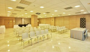 A conference room with rows of chairs, a stage with a podium, and a banner on the wall. - Sercotel Amistad Murcia (Murcia)