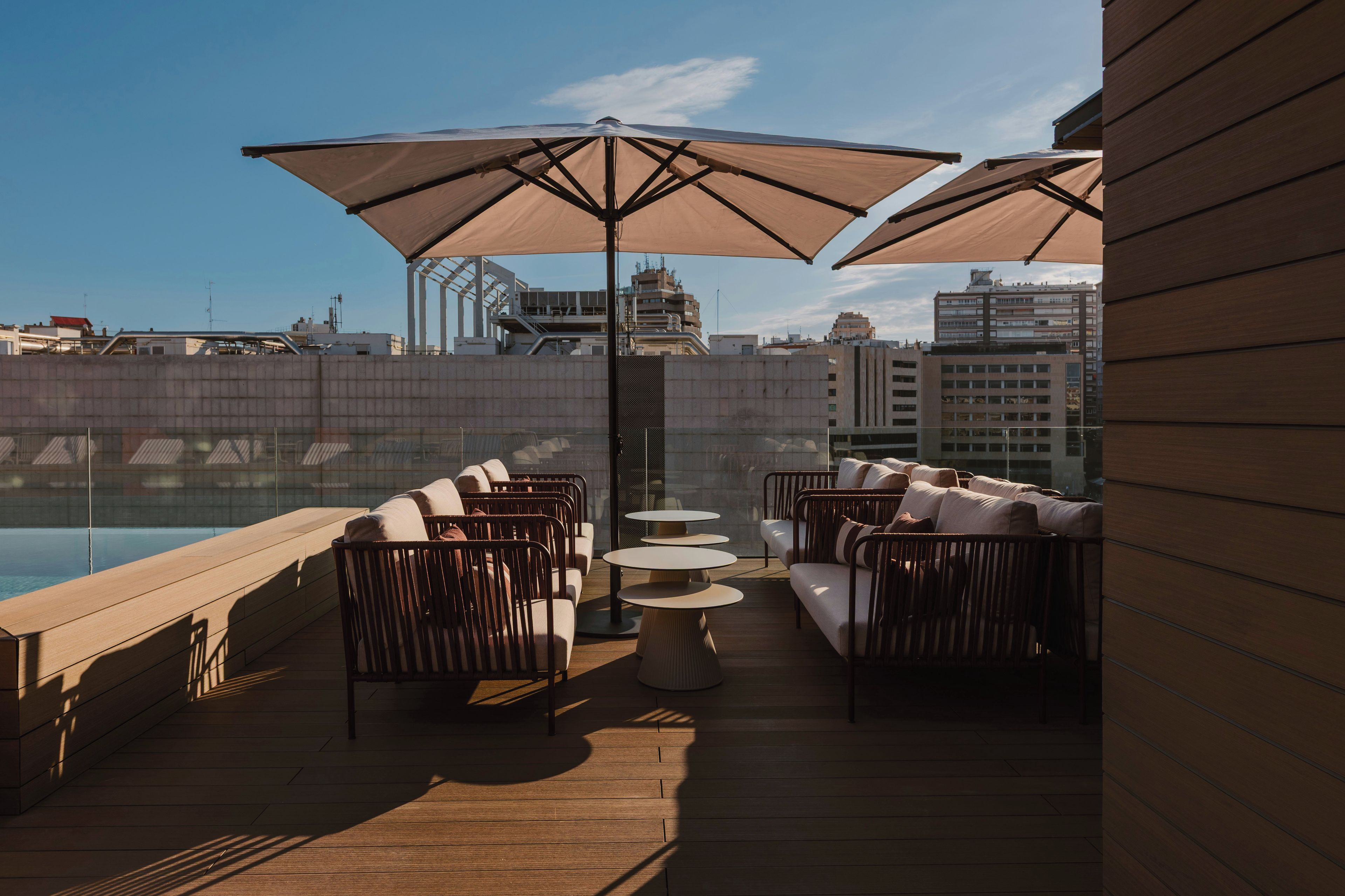 An outdoor seating area with sofas and tables, large umbrellas, and a pool view.