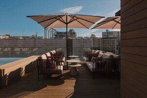 An outdoor seating area with sofas and tables, large umbrellas, and a pool view.