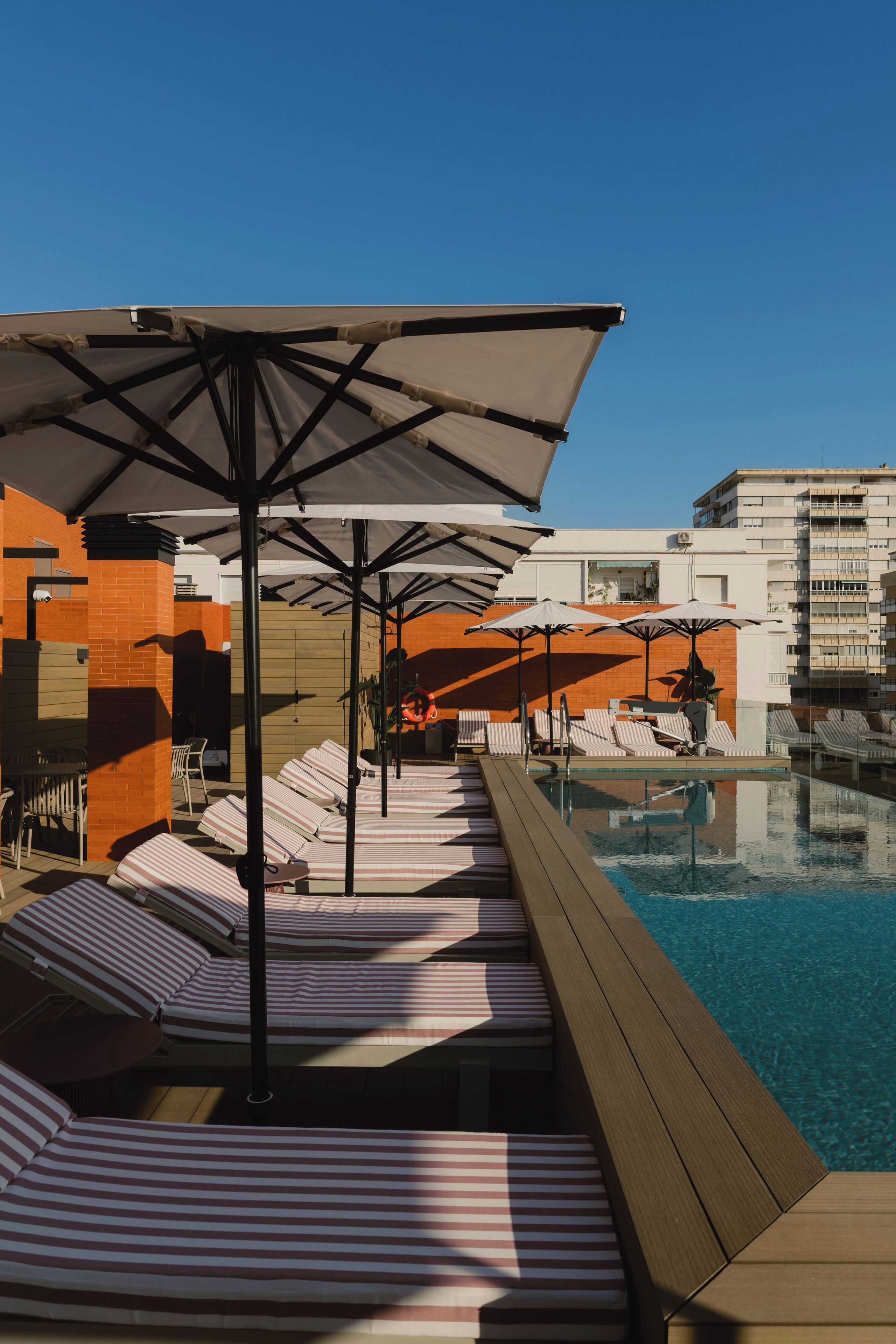 A poolside area with sun loungers and umbrellas, a wooden deck, and a clear blue pool.
