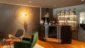 A modern bar area with a round wall light, a bar counter, and a shelf with various bottles. - chic&basic VELVET (Barcelona)