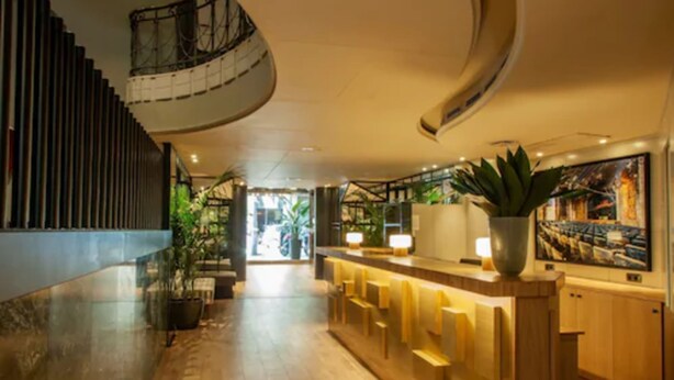 A modern hotel lobby with a wooden reception desk, a spiral staircase, and potted plants. - chic&basic VELVET (Barcelona)