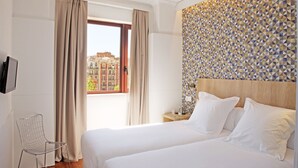 A hotel room with a large bed, a TV mounted on the wall, and a view of buildings through the window. - chic&basic VELVET (Barcelona)