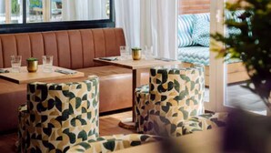 A restaurant with a brown leather booth seating area, patterned chairs, and a view through a window with white curtains. - chic&basic VELVET (Barcelona)