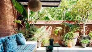 A patio with a brick wall, a blue patterned sofa, and various potted plants. - chic&basic VELVET (Barcelona)