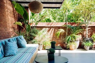 Un patio con un muro de ladrillo, un sofá azul con diseño y varias plantas en macetas.