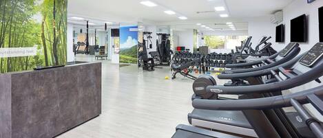 Une salle de sport moderne équipée de tapis de course, d’appareils de musculation et d’un comptoir d’accueil.