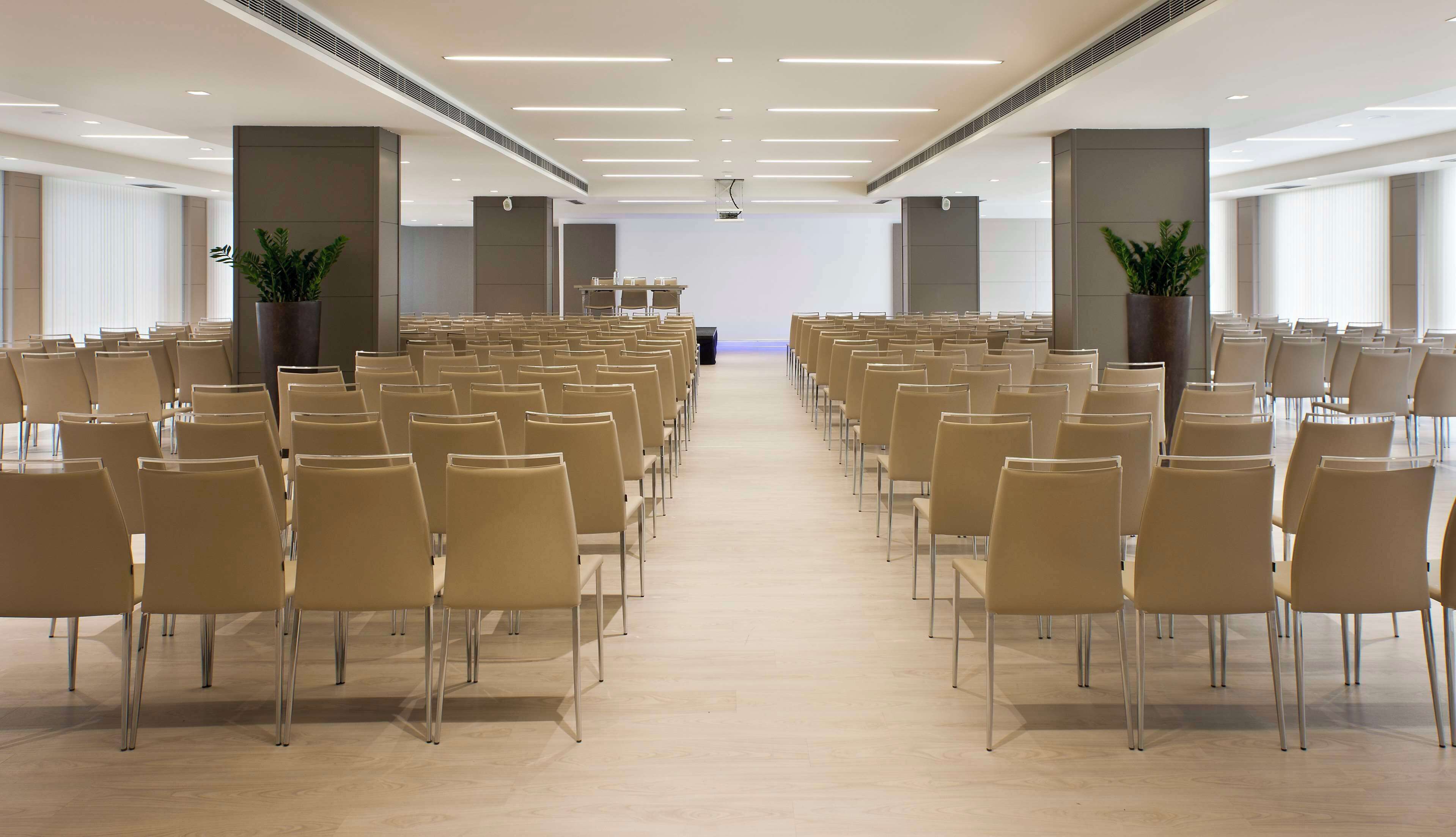 A conference room with rows of chairs, a podium, and potted plants.