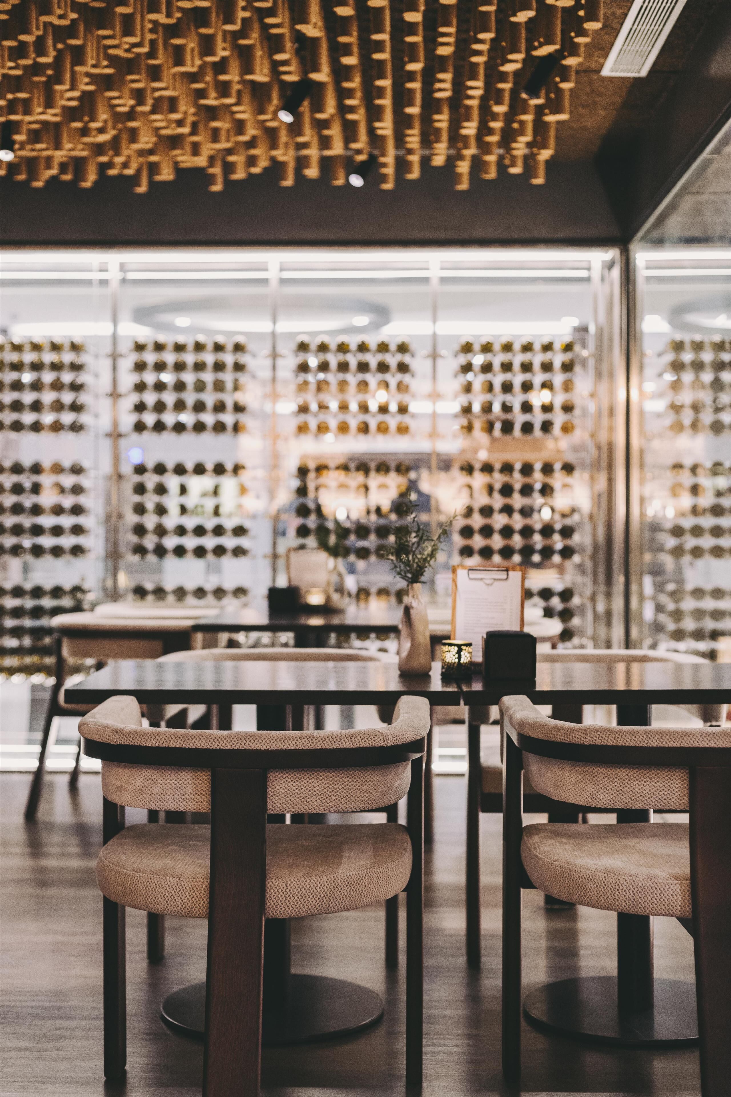 A restaurant interior with a wine display wall, round tables, and cushioned chairs.