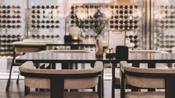 Interior de un restaurante con una pared de exhibición de vinos, mesas redondas y sillas acolchadas.