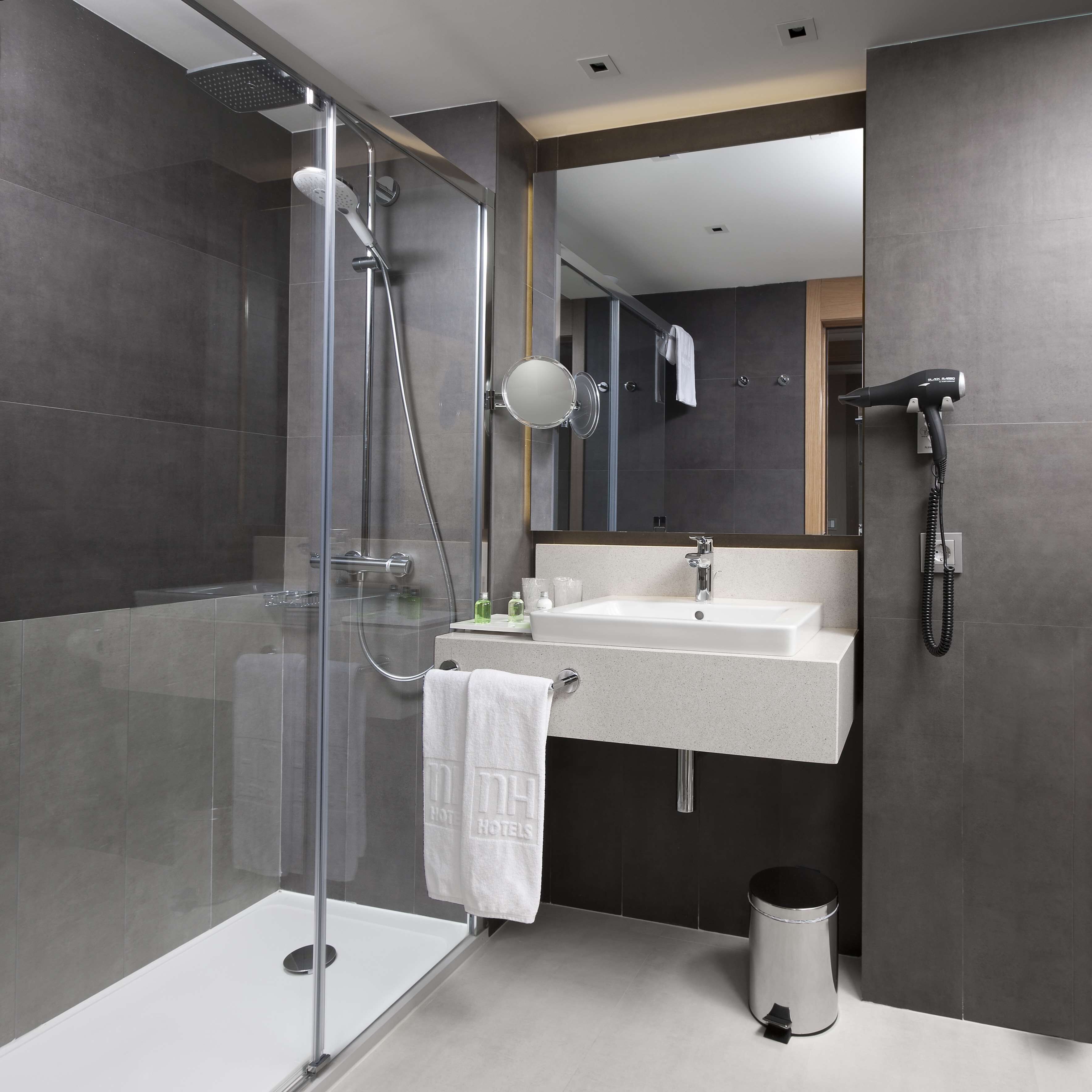 A modern bathroom with a glass-enclosed shower, a sink with a mirror, and a hairdryer on a wall-mounted station.