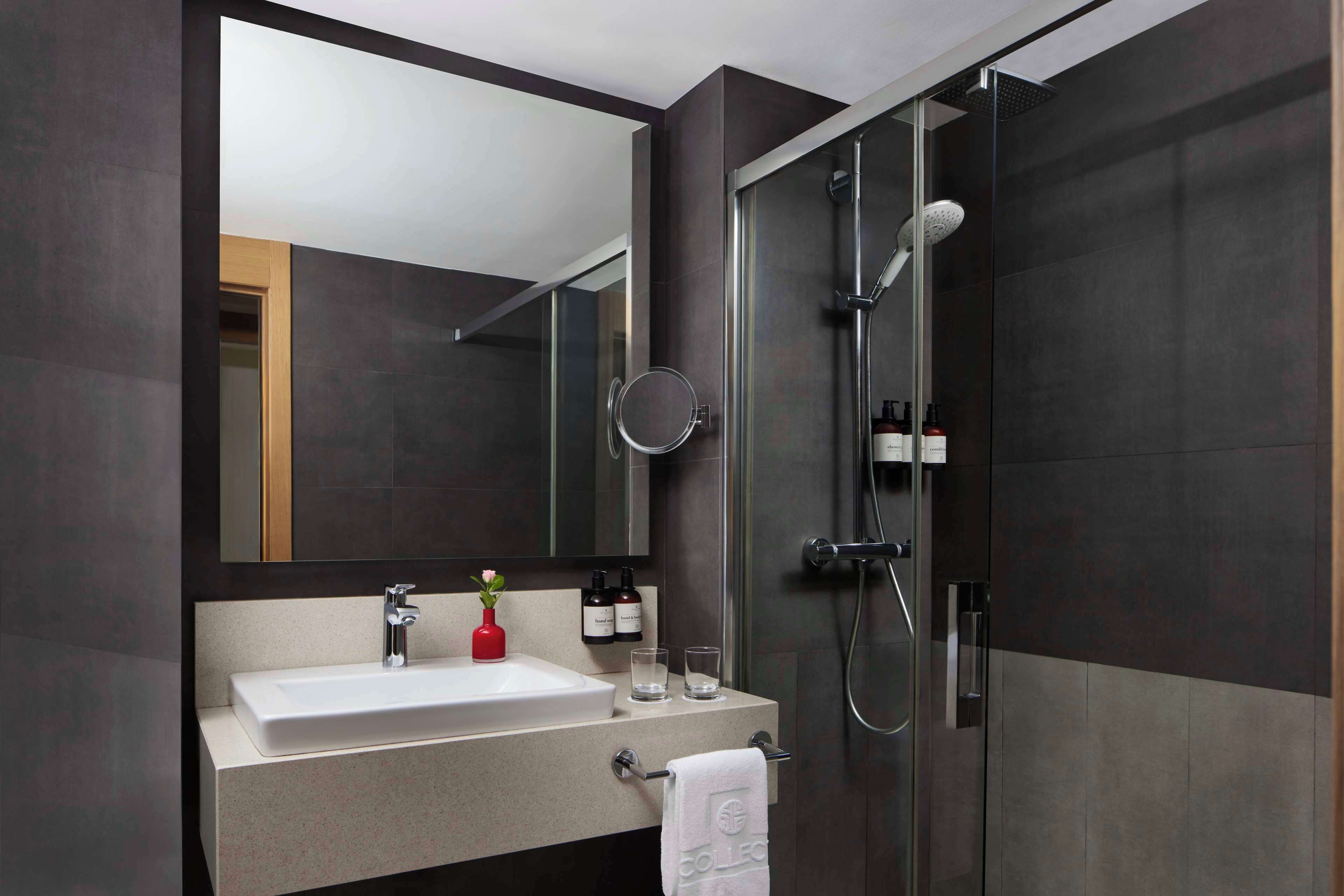 Un baño moderno con un espejo grande, un lavabo, una ducha y un perchero para toallas.