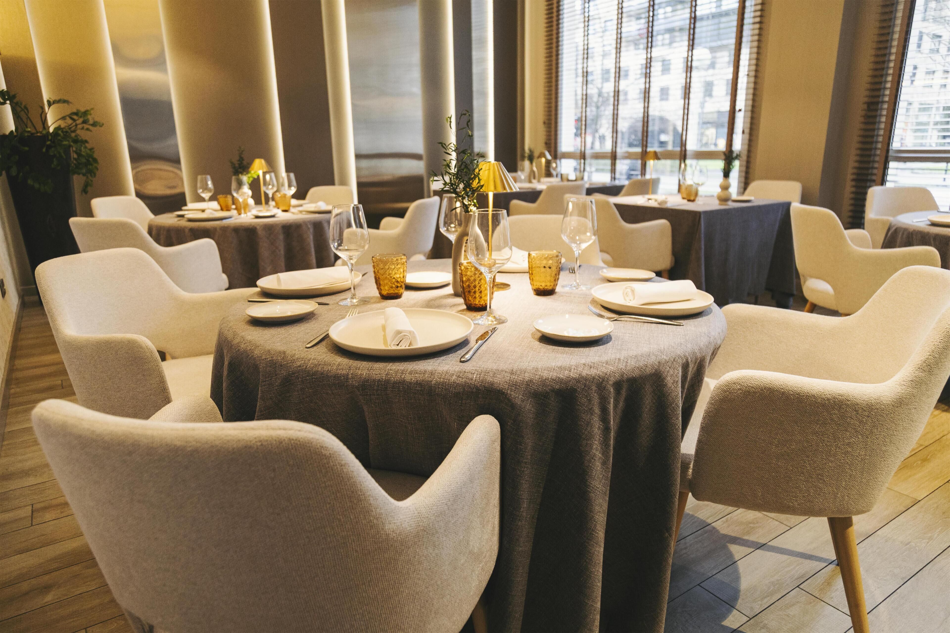 A restaurant with round tables, white chairs, and a modern interior design.