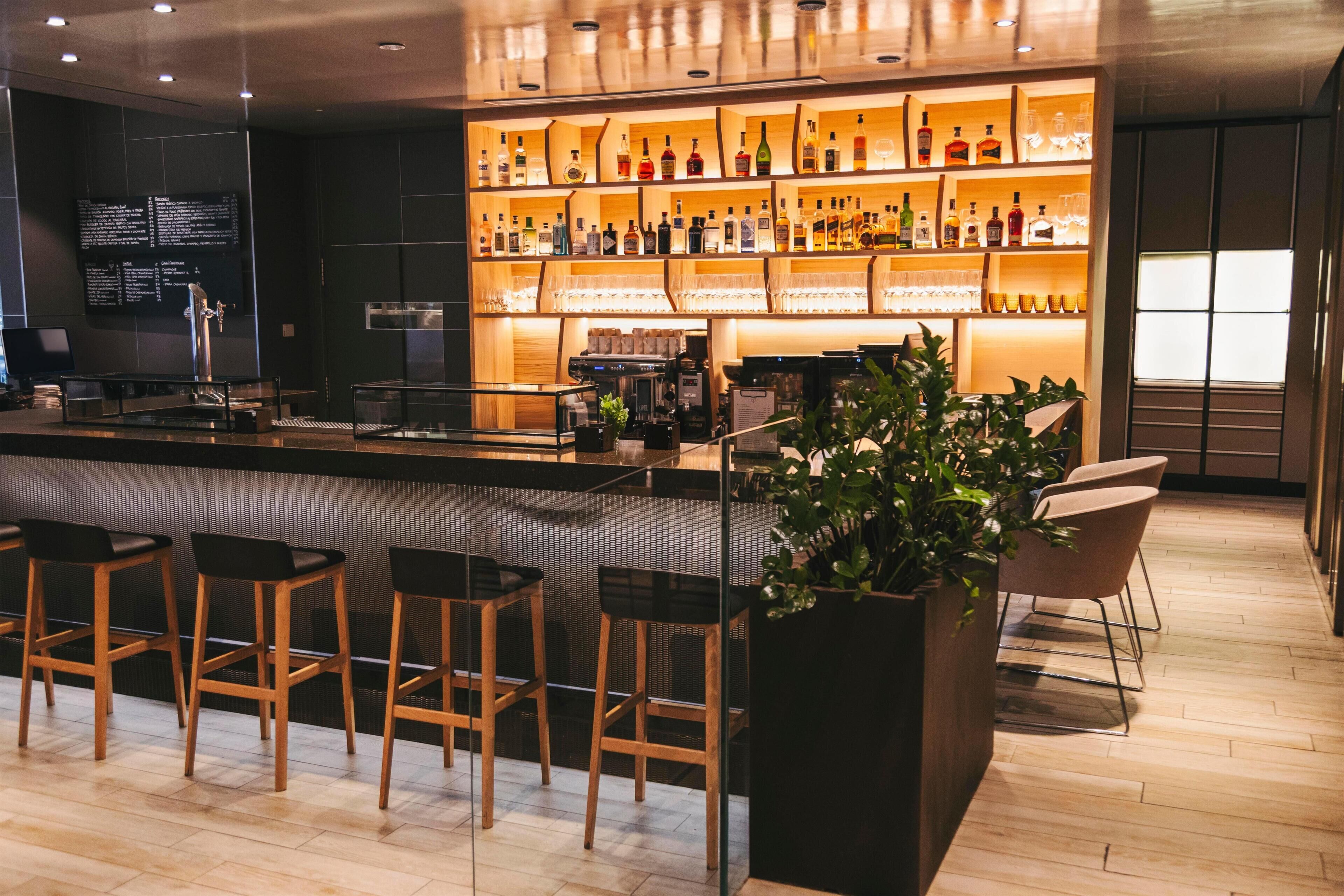 Eine Bar mit mehreren Hockern, einer Theke und einer Auswahl an Flaschen und Gläsern an Regalen.