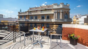 Una terraza en la azotea con una mesa, sillas, una planta en maceta y un edificio al fondo.