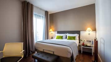 A hotel room with a bed, bedside lamps, a small table with a vase, and a chair.
