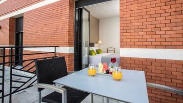 Une chambre d’hôtel avec une façade en briques, un balcon doté d’une table et de chaises, et un plateau de petit-déjeuner avec des fruits et du jus.