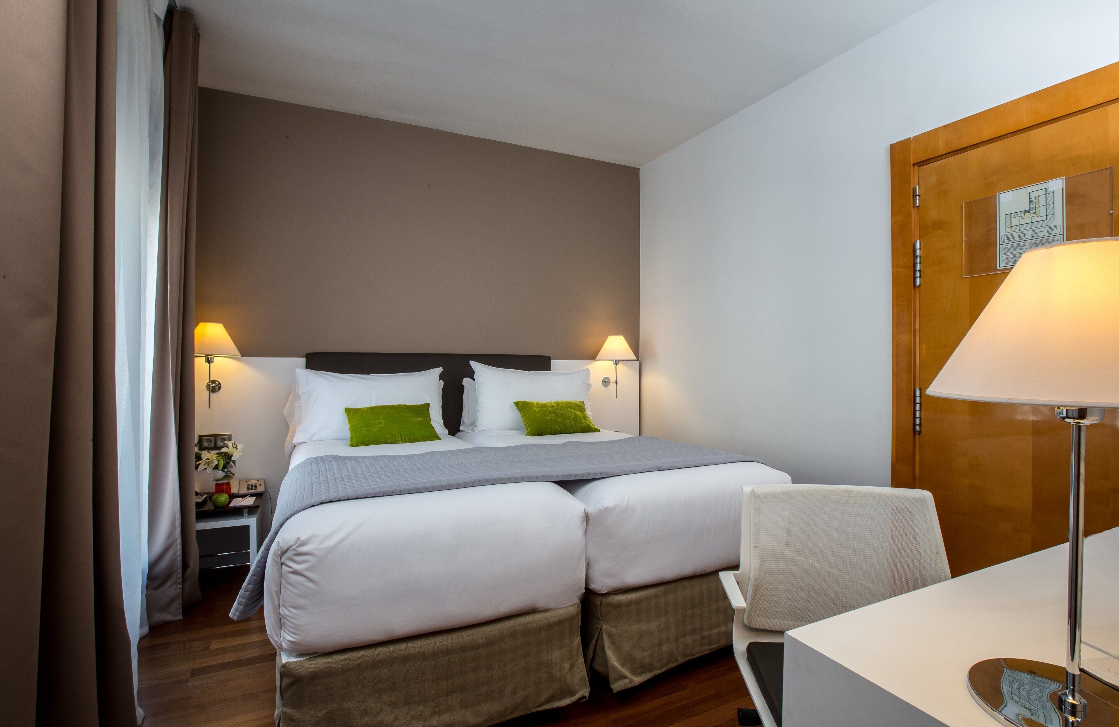 A hotel room with a bed, bedside tables, a desk, and a lamp.