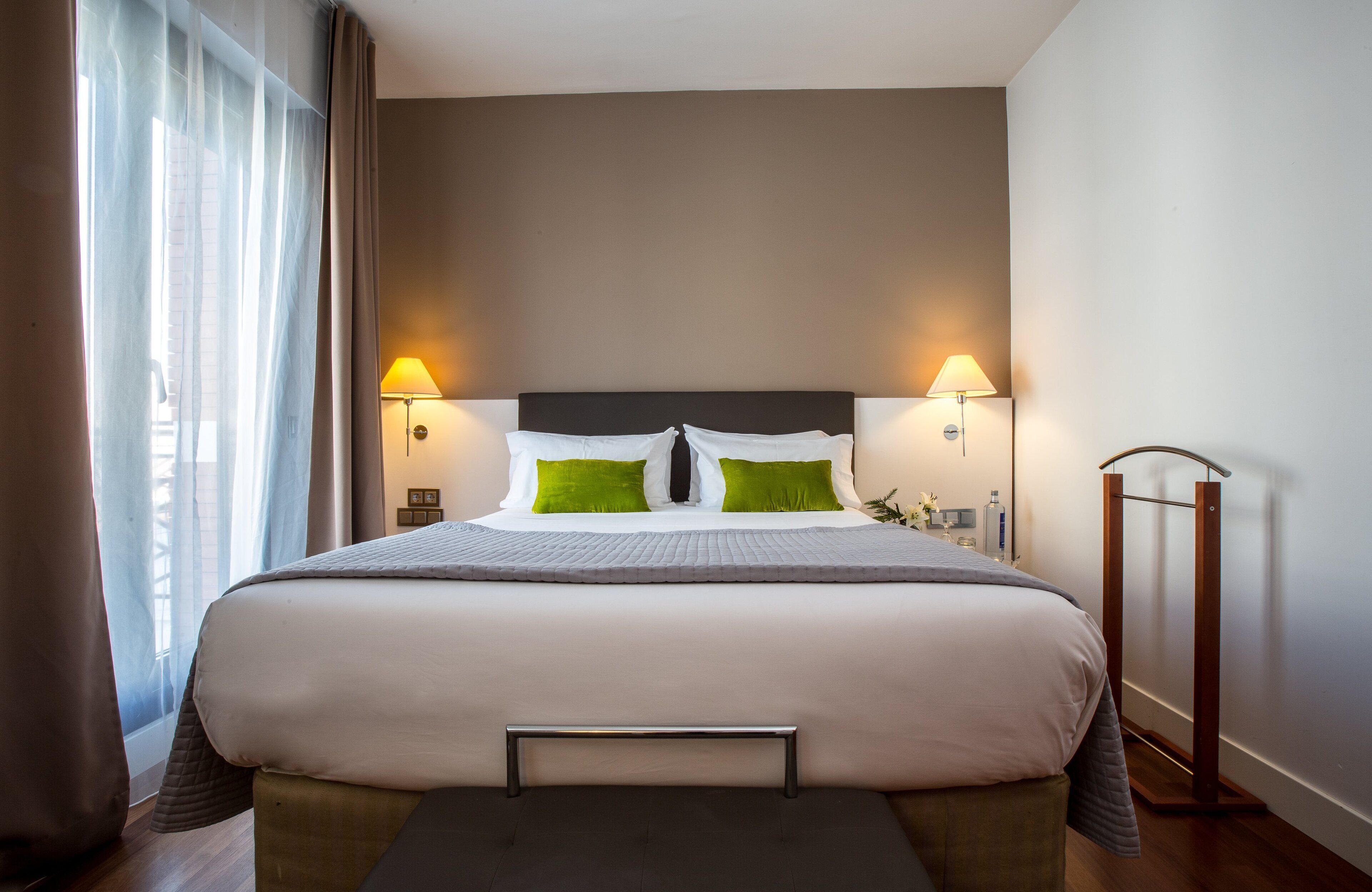 A neatly made bed with a headboard, two bedside lamps, and a bedside table with a lamp.