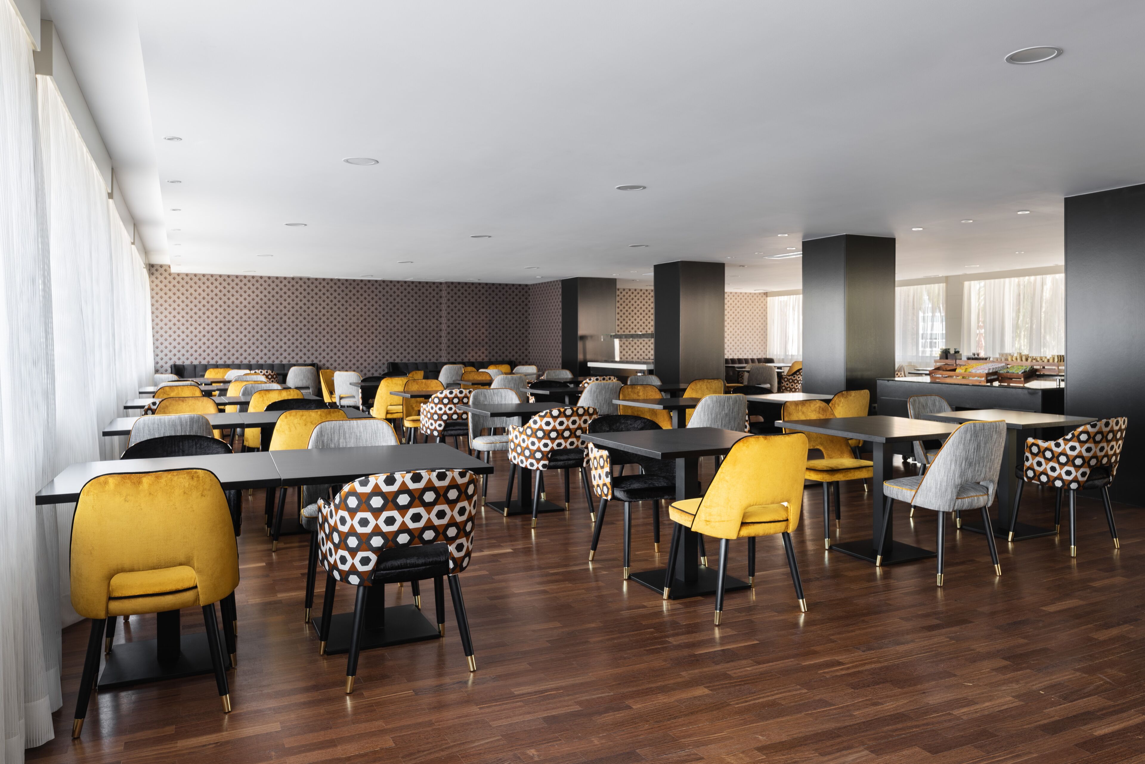 Un comedor amplio con varias mesas y sillas, que presenta un diseño moderno con cojines de estampado geométrico.