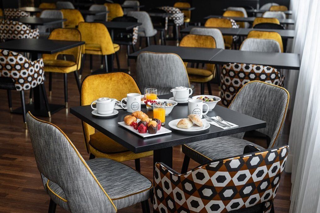 A breakfast setting with a table set for two, featuring a variety of pastries, a glass of orange juice, and multiple cups and plates.