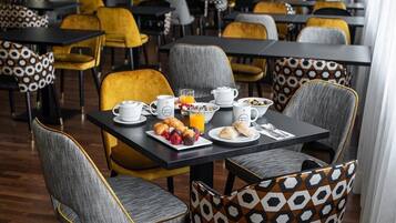 A breakfast setting with a table set for two, featuring a variety of pastries, a glass of orange juice, and multiple cups and plates.