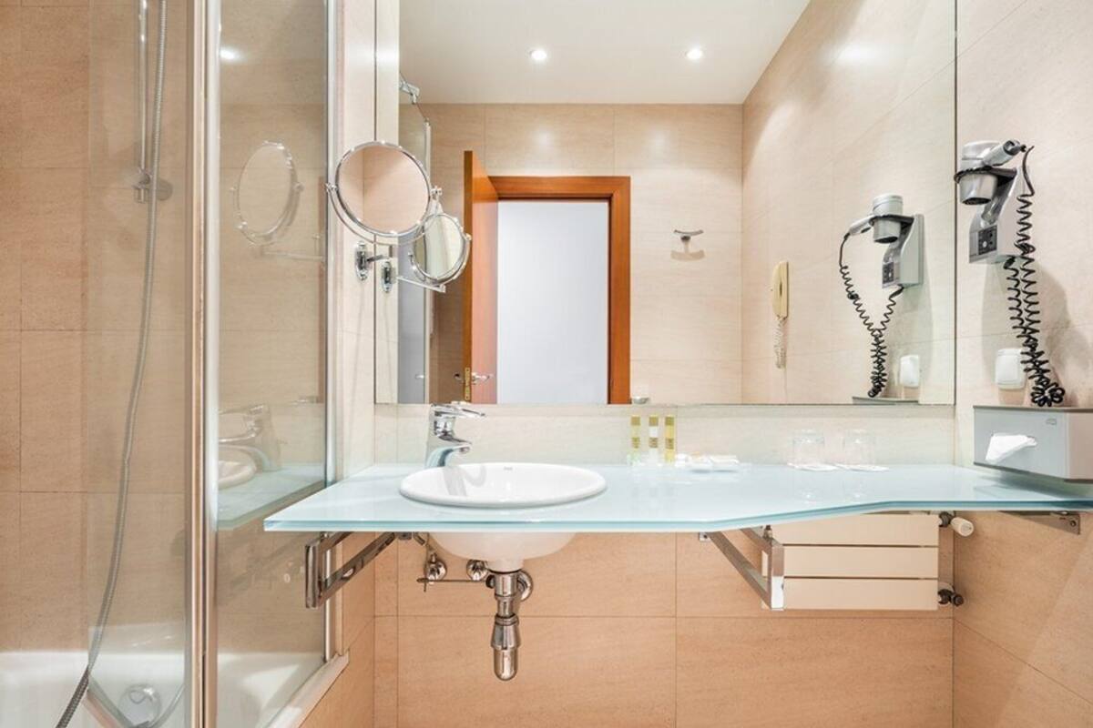 Ein modernes Badezimmer mit einem Glaswaschtisch, einem Handspiegel, einer Handbrause und einem Föhn.