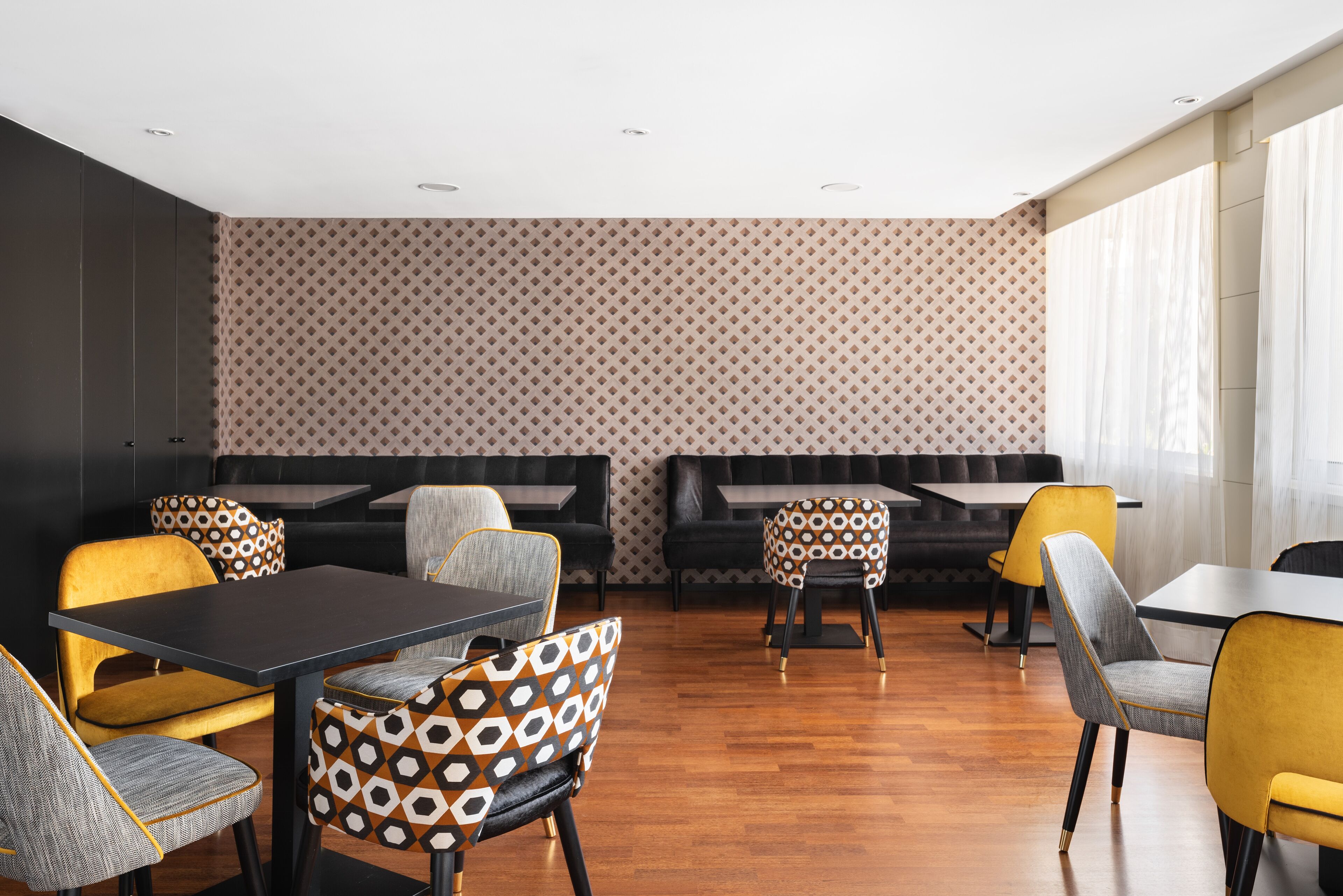 Un comedor moderno con sillas estampadas, mesas negras y amarillas, y un muro con diseño.