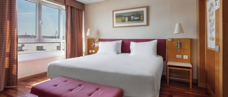 Un cuarto de hotel con una cama grande, un banco, una ventana con cortinas y un cuadro en la pared.