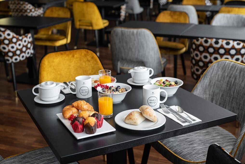 A breakfast setting with a table set for two, including croissants, a fruit plate, a glass of orange juice, and a bowl of cereal.