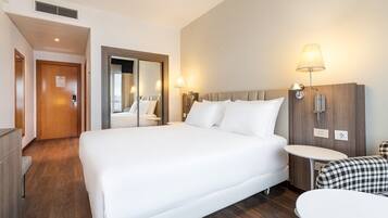 A hotel room with a large bed, a bedside table, a mirror, and a wall-mounted lamp.