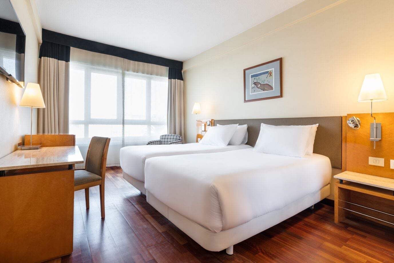 Quarto de hotel com duas camas, uma escrivaninha, uma cadeira e uma janela com cortinas.