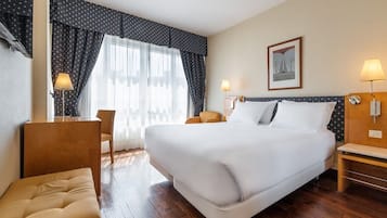 Habitación de hotel con una cama grande, dos mesitas de noche, una silla y un escritorio.
