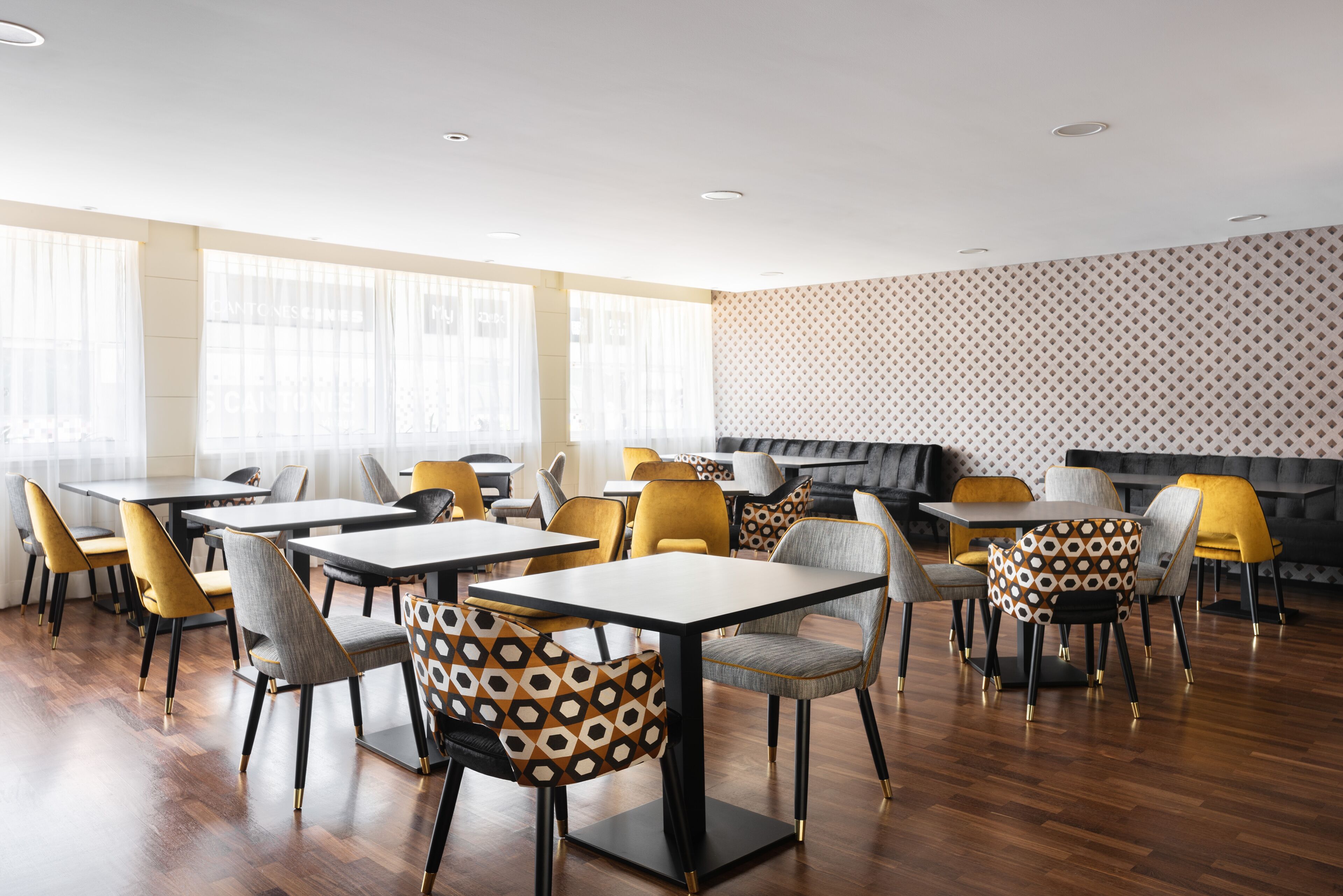 Un comedor moderno con suelo de madera, sillas amarillas y grises, y una pared con estampado.